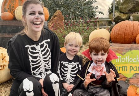 Woman and two children in halloween fancy dress smiling in front of pumpkins