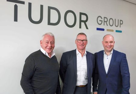 3 business men in front of a sign that reads 'tudor group' represnting tudor business solutions