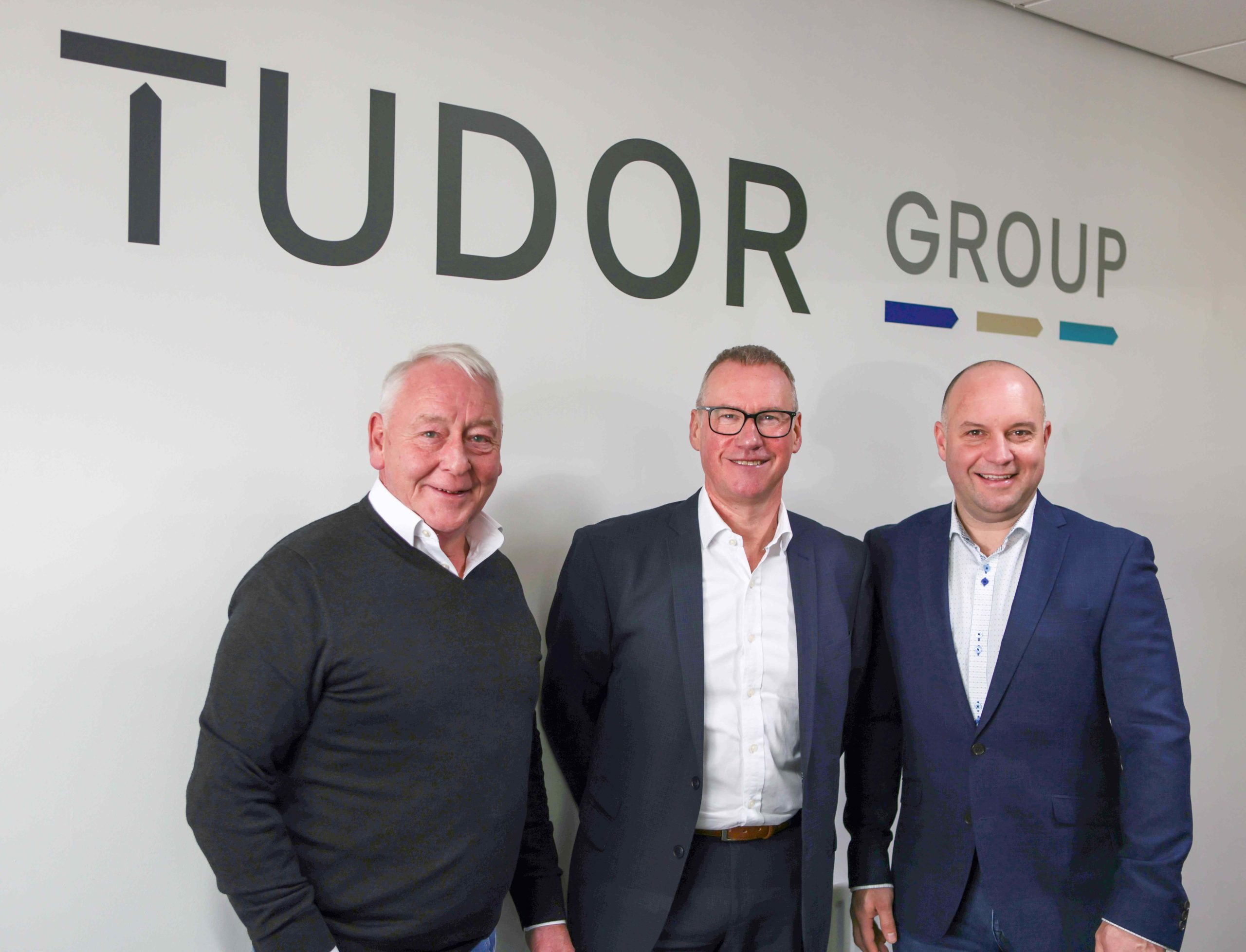 3 business men in front of a sign that reads 'tudor group' represnting tudor business solutions