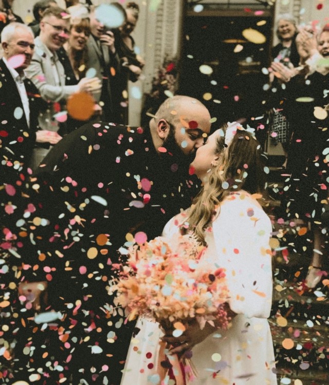 Bride and groom kissing with crowd throwing confetti