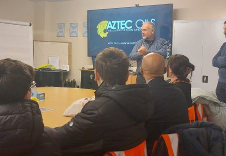 Students listening to a man speak in front of an Aztec Oils sign
