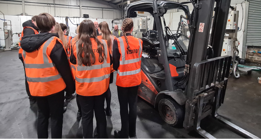 Group of students in high vis jackets in a warehouse