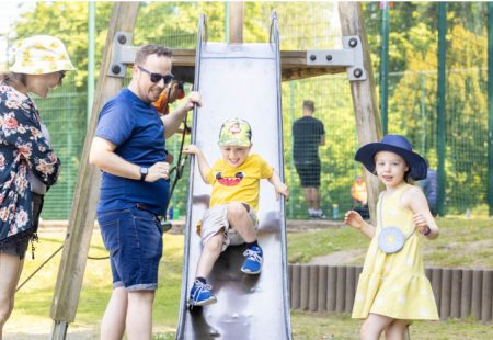 Man, woman and girl watching a boy go down a slide