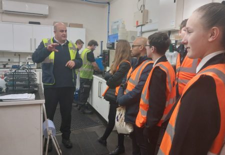 Group of students in high vis jackets in a work space
