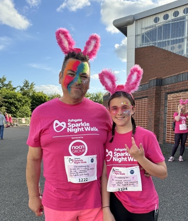 Man and girl in pink t shirts and bunny ears. Man is waering colourful facepaint