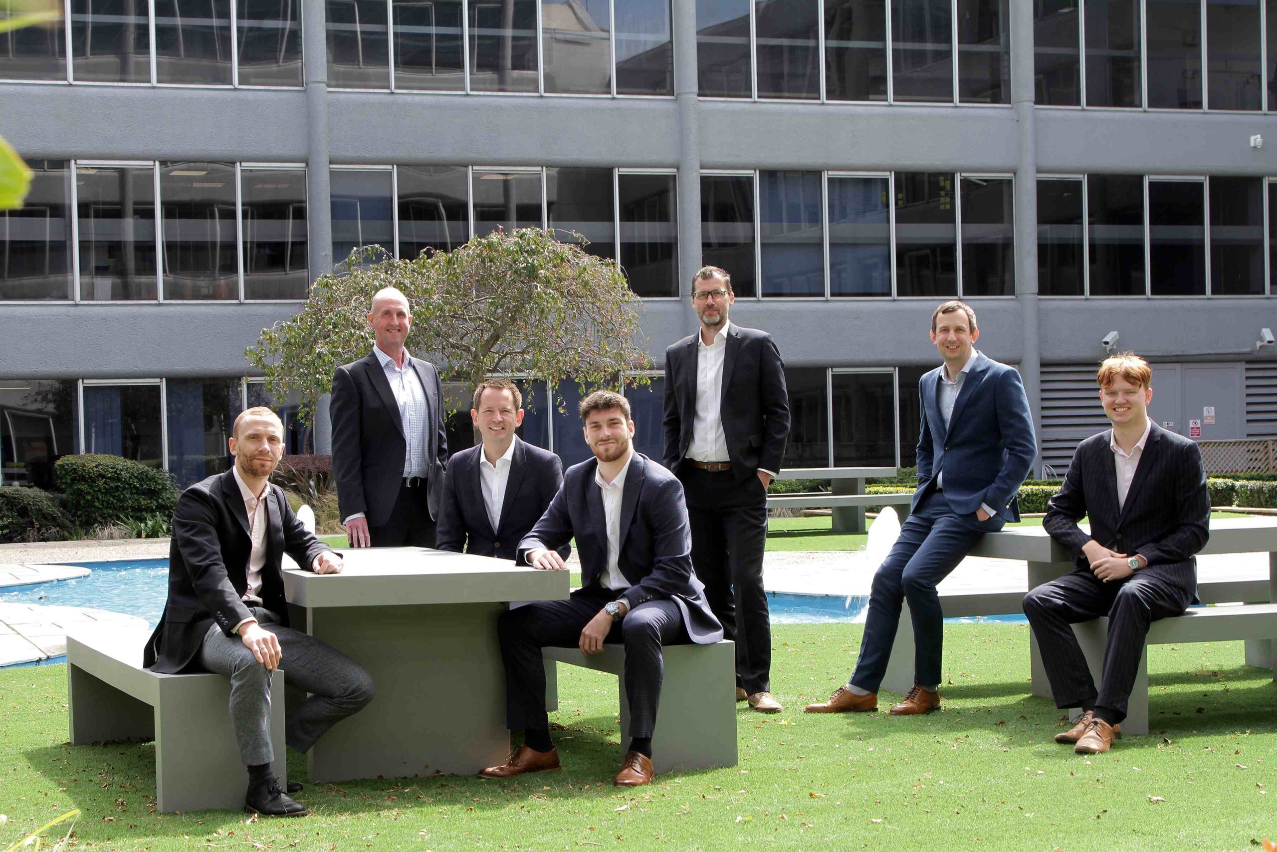 7 males in suits sat around benches in an office garden, representing the team at FHP Property Consultants