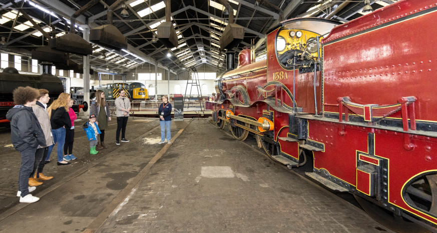 Group of people in a warehouse looking at an old fashioned train