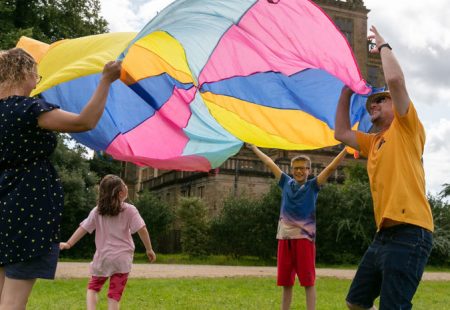 Man, woman, boy and girl playing with a colourful parachute outside