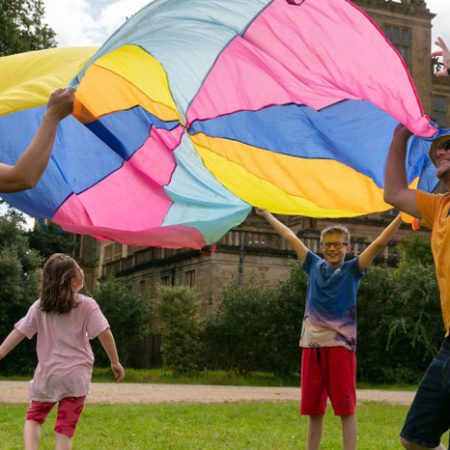 Man, woman, boy and girl playing with a colourful parachute outside