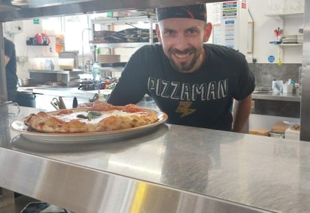 Pizza chef in Italian restaurant places a pizza over the pass ready for service