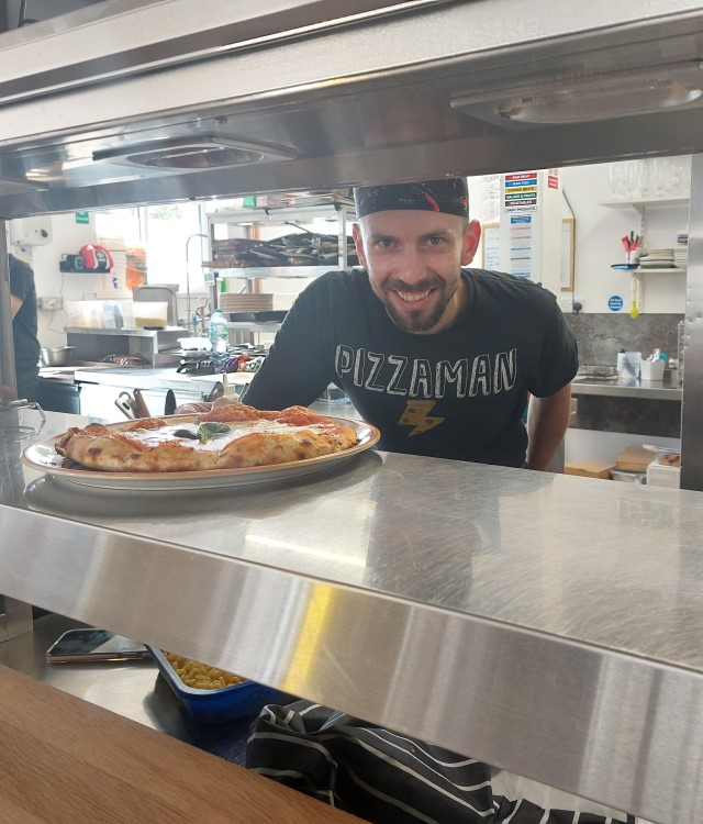 Pizza chef in Italian restaurant places a pizza over the pass ready for service