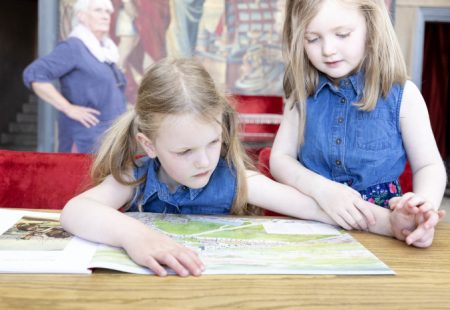 Two young girls sitting at a table looking at a large book