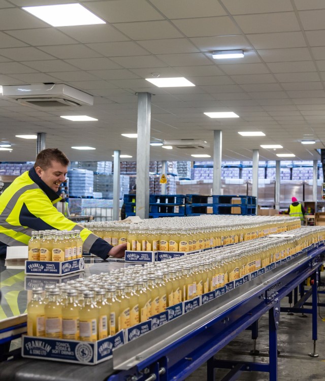 Global Brands drinks factory - bottles on production line being handled by male in high visibility clothing