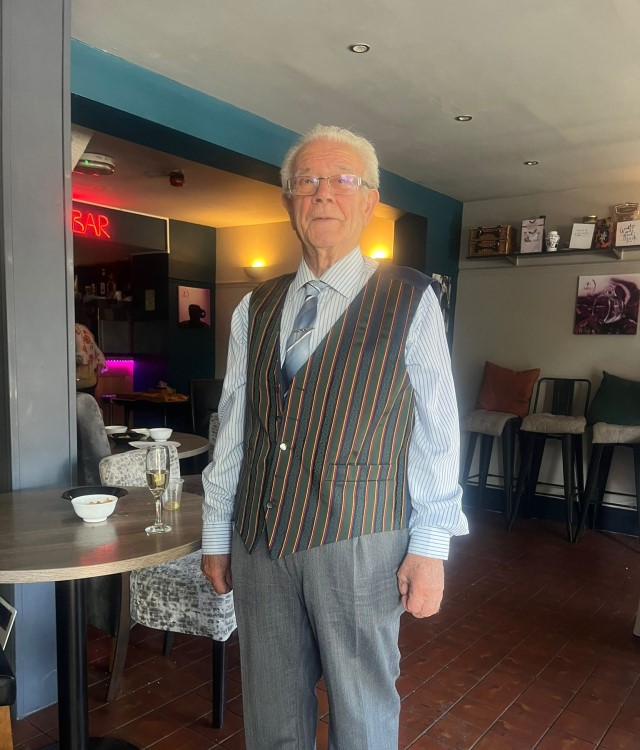 Man with white hair stood in restaurant wearing smart clothing