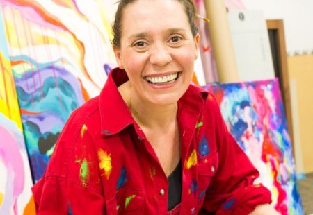 Artist wearing red overalls with paintings in background