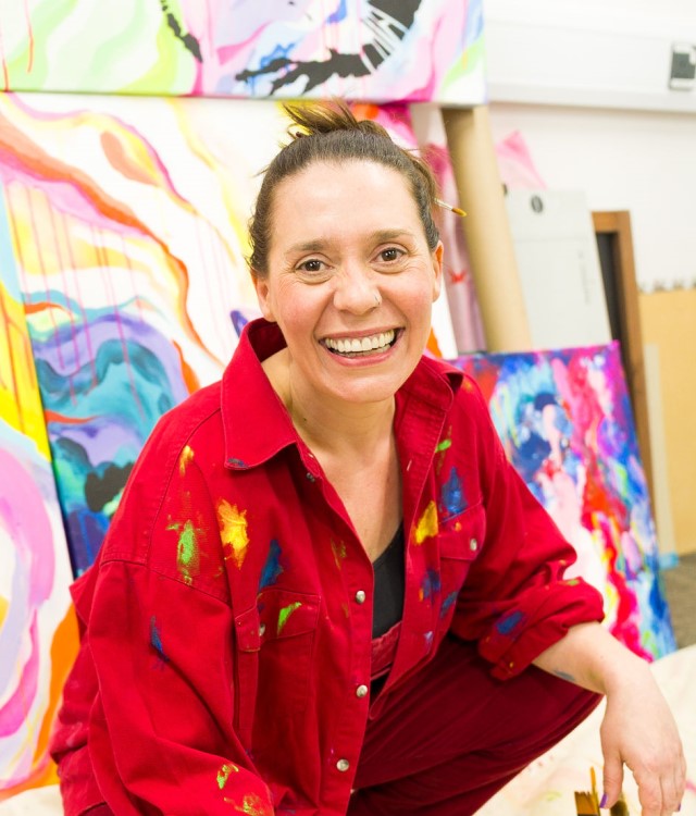 Artist wearing red overalls with paintings in background