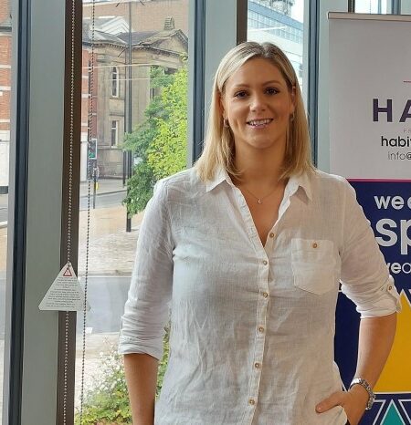 Woman in white shirt stood in front of window and banner