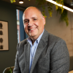 A man smiling at the camera in a grey suit jacket and blue shirt - David Wells, Director at HBD