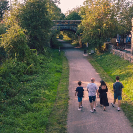 Family walking along a path surrounded by grass and next to a building with arch windows