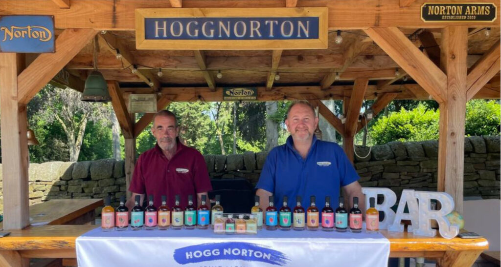 Hogg and Norton stood behind bar displaying drinks