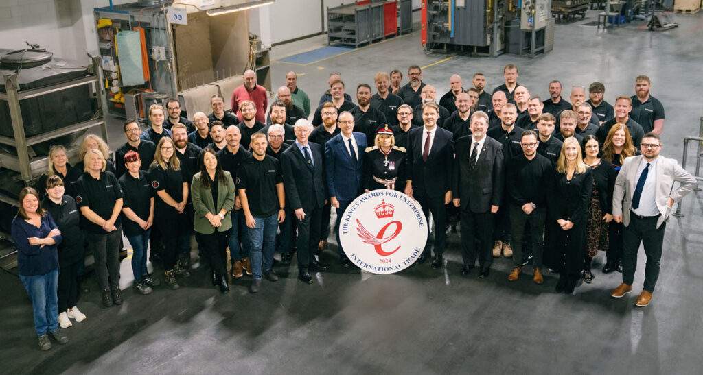 Large group of people in company uniform pose for a photo. Image taken from above in large warehouse space