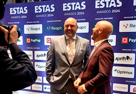 Photographer takes picture of two men in suits in front of award banner