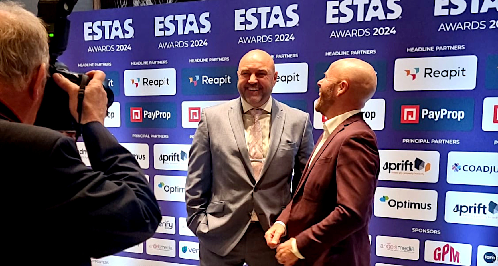 Photographer takes picture of two men in suits in front of award banner