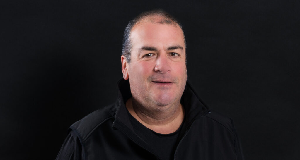 Male smiling for camera in front of dark background