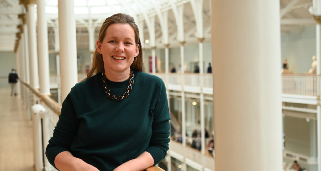 Woman stood on balcony in large open hallway smiling