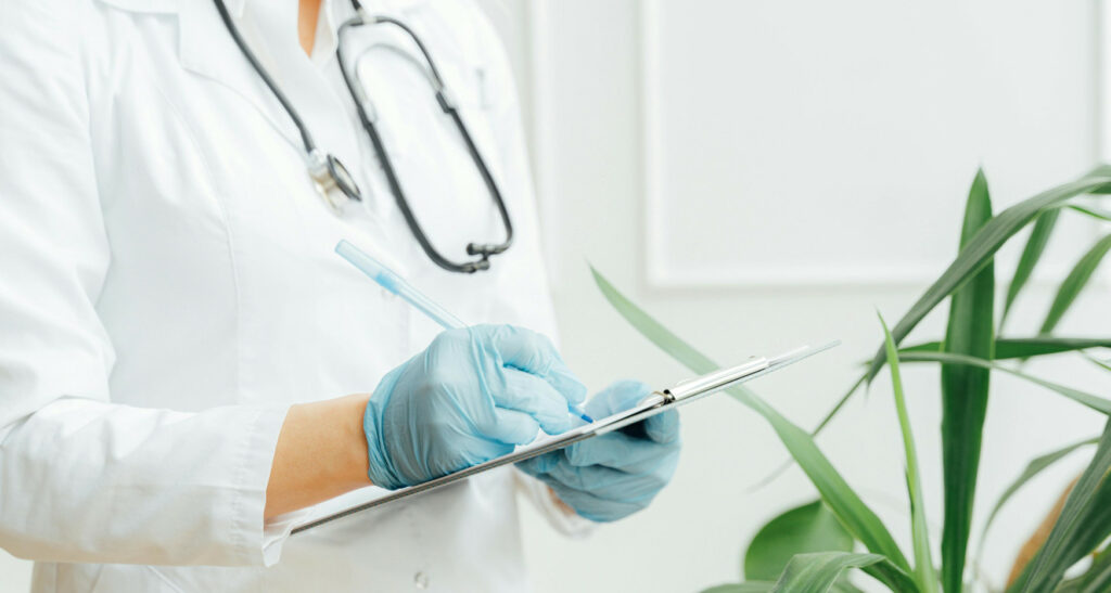 Doctor writes on clipboard wearing stethoscope and gloves